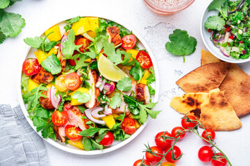 Gourmet salad with grilled chicken and mango salsa, tomato, cilantro, onion and lettuce in mexican style, white kitchen table background, top view