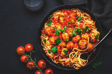 Prepared spaghetti pasta with fried pork meatballs in tomato sauce with parsley in frying pan, black table background, top view