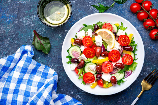 Tasty Greek salad with feta cheese, kalamata olives, tomatoes, paprika, cucumber and onion, healthy mediterranean food. Blue table background, top view