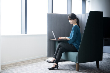 会社の窓際でパソコンを開いて働く日本人女性　全身