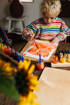 Creative boy painting a dinosaur with crayons and watercolor paint