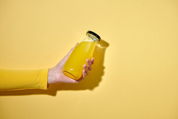 Female hand with a bottle of juice on color background