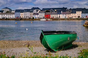 A green boat at shore with Galway's skyline in the background