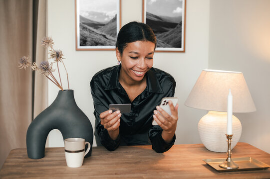 Happy Woman With Credit Card Using Smartphone At Table