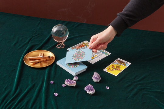 Tarot reader taking cards, magic sphere and stones beside.