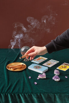 Woman holding incense sticks with tarot cards beside.