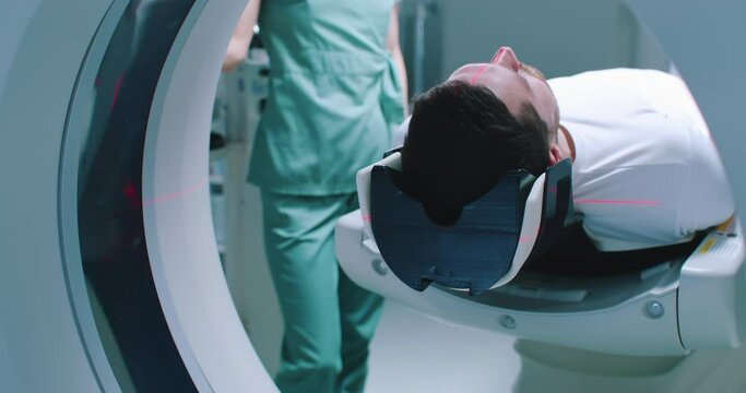 Close-up back shoot of male patient after magnetic resonance imaging. Man is going out of MRI machine. Doctor is finishing tomography procedure. Tomography under infrared rays.