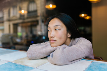 Dreamy Asian woman leaning on table in cafeteria