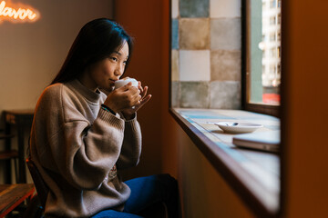 Calm Asian woman drinking hot coffee in cafe