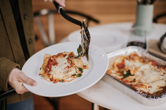 Woman serves a portion cooked lasagna from a tray.