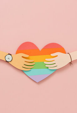 Different color hands holding colorful heart LGBT flag