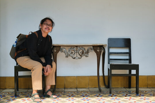 A middle-aged woman in black shirt is sitting on a wooden chair; happy expression