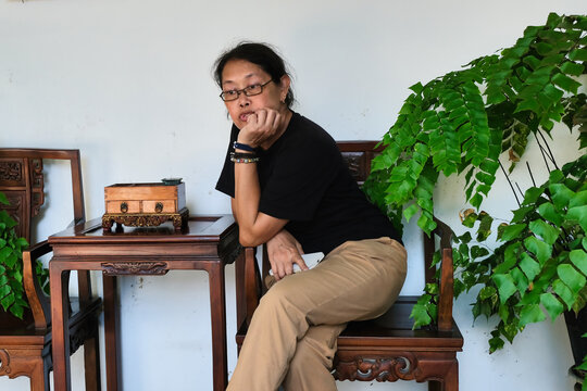 A middle-aged woman sitting in a wooden chair; thinking, serious expression