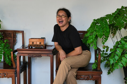 A middle-aged woman sitting in a wooden chair; laughing, happy expression