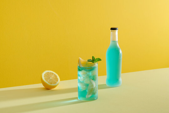 Glass of Blue Lagoon cocktail on light background with bottle