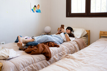 Teen girl chilling with phone and headphones on Bed