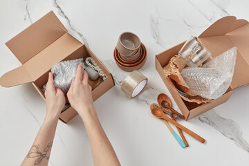 Girl putting wrapped kitchenware in cardboard boxes.