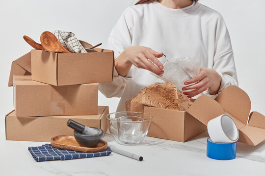 Female entrepreneur putting glassware in cardboard packages.