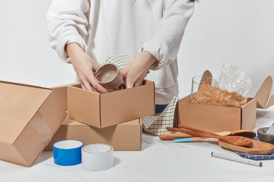 Woman accurately putting dishware in open boxes.