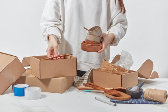 Young woman holding dishware over open cardboard boxes.