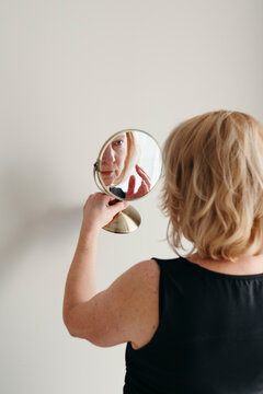 Mature woman looks at herself in mirror.