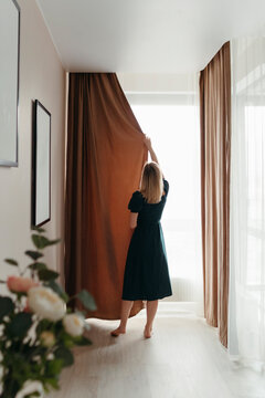 Woman closes curtain on large window.
