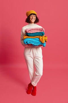 Cheerful lady with stack of knitted scarves in studio