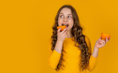 happy teen girl eating orange fruit on yellow background