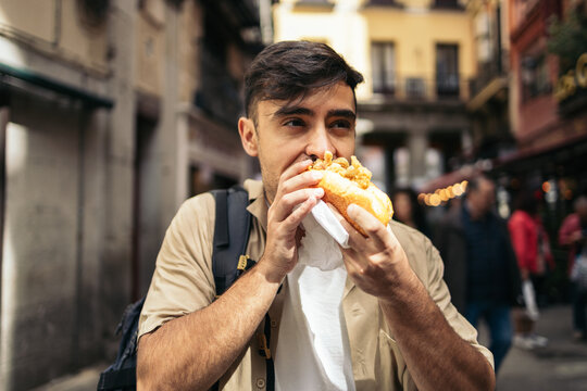 Young man visiting Madrid eating a typical calamari sandwich.