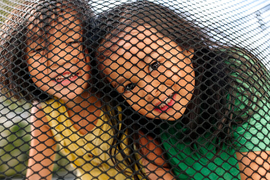 Smiling sisters looking through the net of a trampoline 