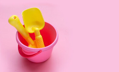 Plastic toys, shovels in bucket on pink background. Summer background concept
