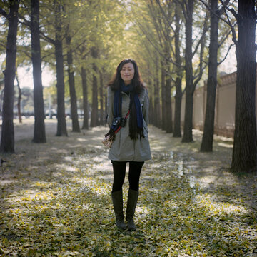 A woman stands between two rows of ginkgo trees