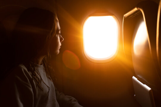 Girl looking out a plane window as light streams in