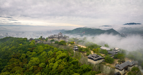 Fog and mist over historic Japanese castle on hilltop by city at dawn