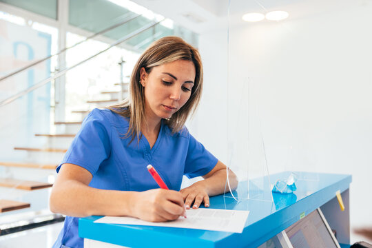 Young woman writing information on paper in clinic