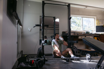 Tired workout guy drinking on the floor during exercise routine.