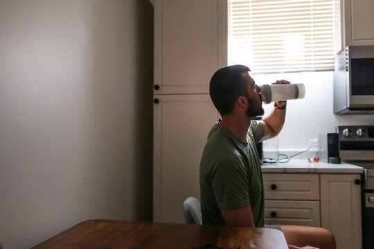 Man drinking from shaker cup in the kitchen before workout.