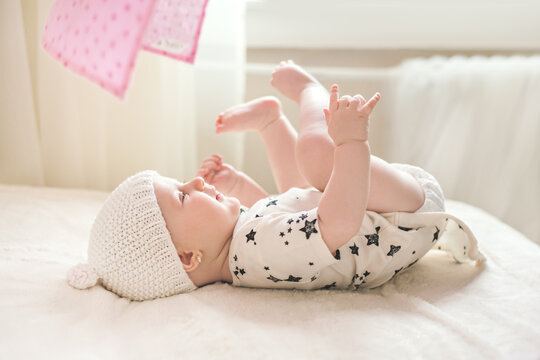 Baby on a bed playing with her own hands and feet. 