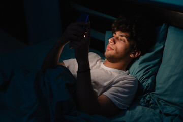 Cell phone addict man awake late at night in bed using smart phone checking likes and followers on...