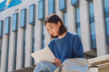 Focused Asian student writing notes near university