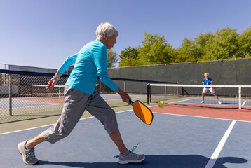 Senior Citizen Pickleball player on reaches to return ball on court
