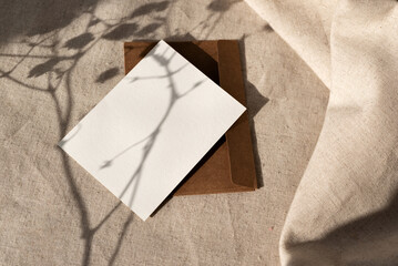 Empty paper card and envelope with aesthetic harsh floral sunlight shadows on neutral beige linen...