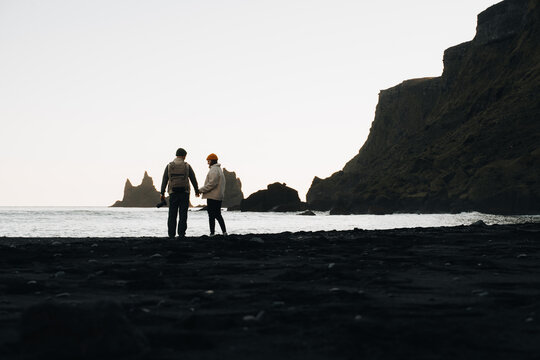 Couple holding hands on black sand beach Reynisfjara with ocean waves - Powered by Adobe