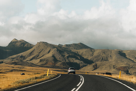 Car driving on a road through volcanic mountains and fields.