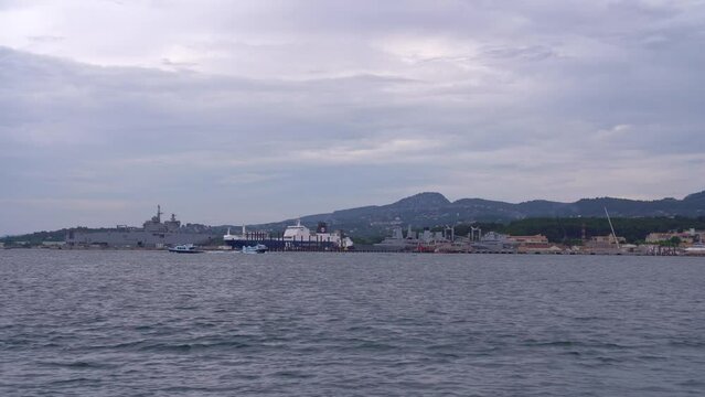 Harbor with moored war ships of French Navy with mountain panorama in the background on a cloudy late spring day at City of Toulon. Movie shot June 9th, 2023, Toulon, France.