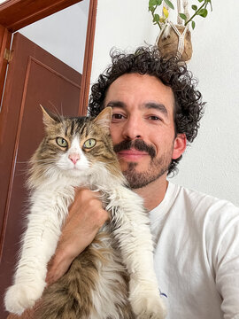 A selfie of a man with curly hair and a beard carrying his cat