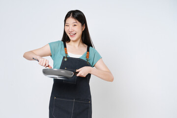 Young woman wearing kitchen apron cooking and holding pan and spatula isolated on white background.