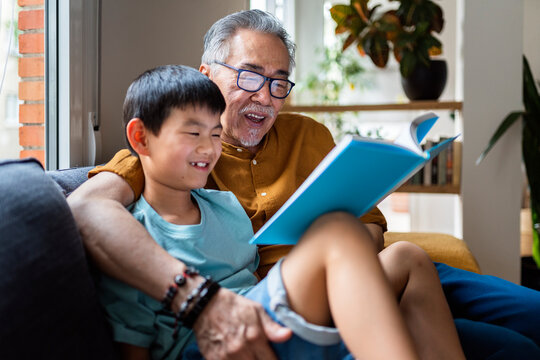 Grandpa reading book to smiling grandson.