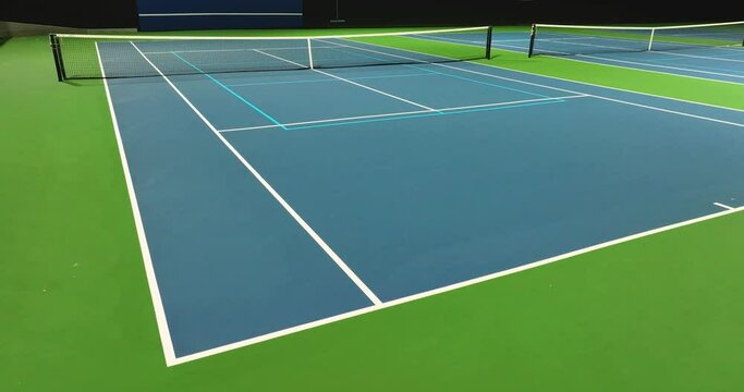 Evening video of outdoor blue tennis courts with pickleball lines with lights turned on.	