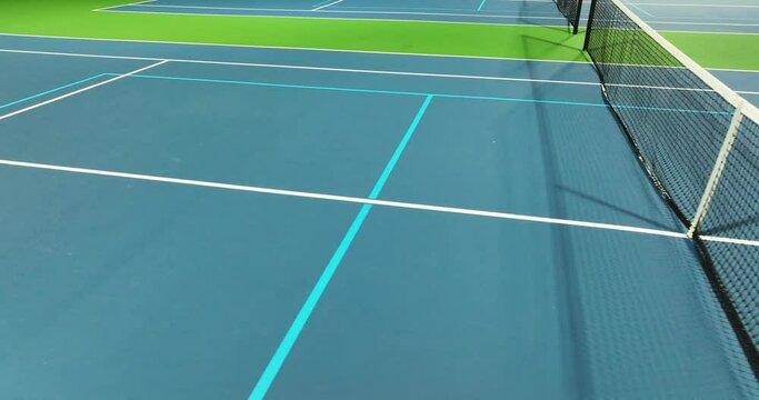 Evening video of outdoor blue tennis courts with pickleball lines with lights turned on.	